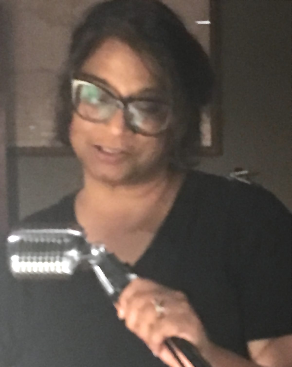Dark skinned woman with bobbed hair and oversized glasses, holding a microphone while reading.